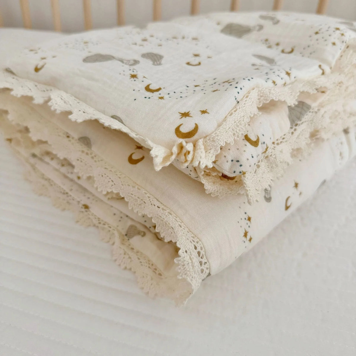 A folded white muslin baby blanket with gold star and crescent moon embroidery resting on a white surface.