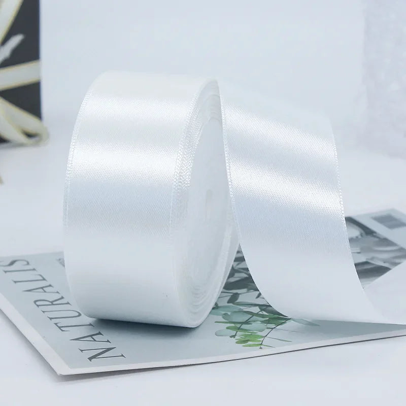 A roll of white satin ribbon used for gift wrapping or DIY crafts, lying on a sheet of paper.