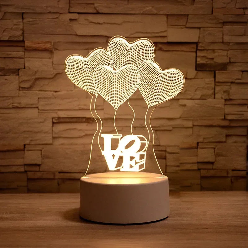A glowing LED night light lamp shaped like three heart-shaped balloons with the word LOVE inside on a wooden surface.