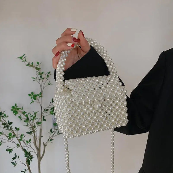 Una mano sostiene un bolso cruz blanco adornado con perlas contra un fondo claro.