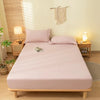 A light pink fitted bed sheet set with pillows on a wooden bed frame in a bright room.