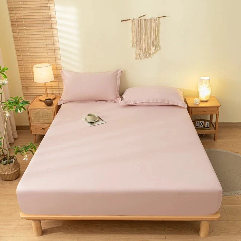 A light pink fitted bed sheet set with pillows on a wooden bed frame in a bright room.