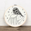 A black line drawing of a woman with long, wavy hair and flowers on her head, ready for floral cross stitch embroidery.