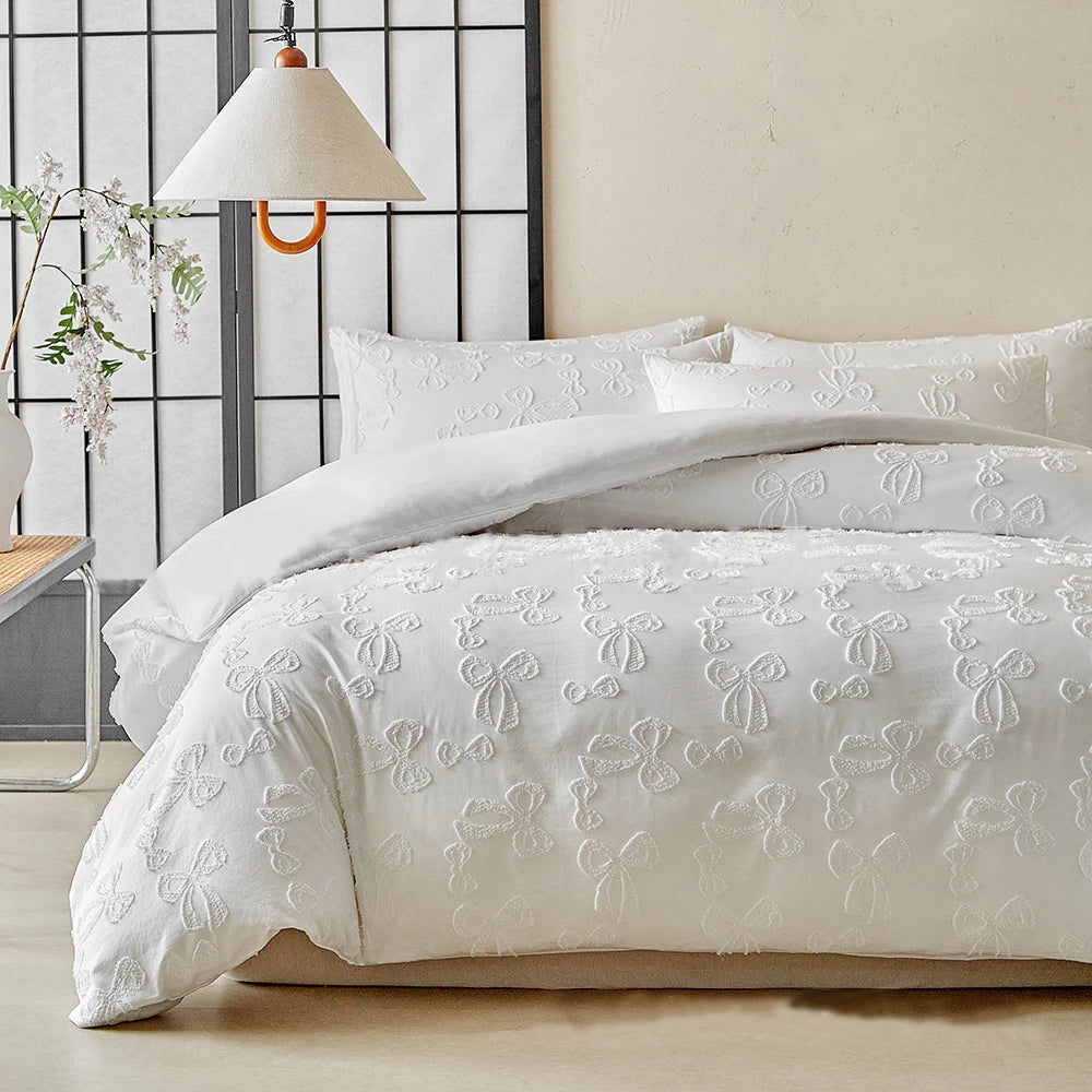 White duvet cover set with delicate embroidered leaf patterns on a bed against a light wall and a black grid background.