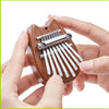 A hand holds a wooden kalimba thumb piano with metal tines, showing the instrument's design.