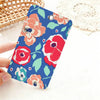 A hand holds a blue floral card holder keychain featuring pink and red flowers on a white background.