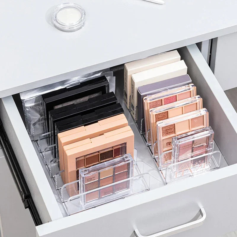 Klares Acryl-Organizer mit Make-up-Produkten wie Lidschattenpaletten und Lippenstiften in einer weißen Schublade.