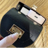 A close-up of a black mini floral textured crossbody tote bag with a gold clasp and a white phone inside.