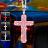 A pink rhinestone cross pendant on a silver chain displayed against a blurred car interior background.