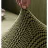 A hand is stretching a textured olive green quilted fabric, demonstrating the elasticity of the material.