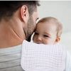 A baby is being held by a man and covered with a white muslin burp cloth.