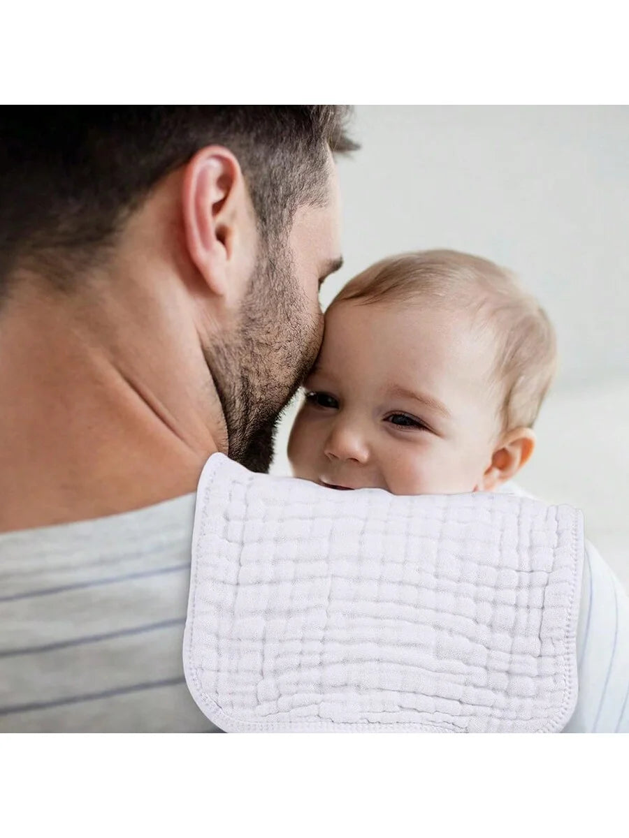 A baby is being held by a man and covered with a white muslin burp cloth.