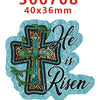 A teal acrylic hair bow decoration featuring a gold cross design with green foliage and the text He is Risen.