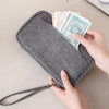 A hand is opening a gray RFID-blocking passport holder filled with cash and travel documents.