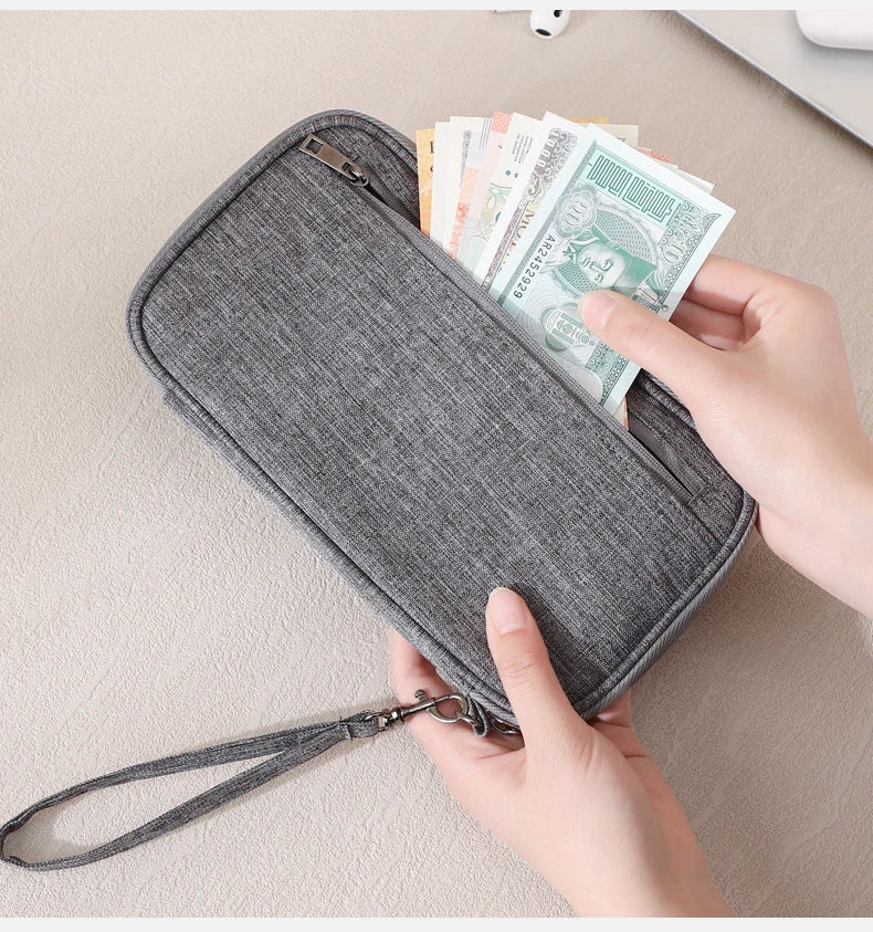 A hand is opening a gray RFID-blocking passport holder filled with cash and travel documents.
