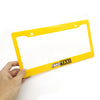 A hand holds a yellow racing style license plate frame with the text FAKE TAXI on it.
