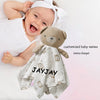 A smiling baby holding a gray stuffed bear comforter with the name JAYJAY on it.