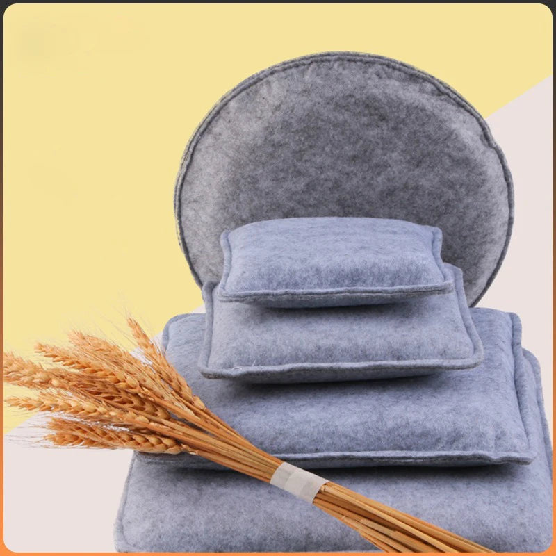 A stack of blue gray needle felting mats rests on a surface next to a bundle of golden wheat.