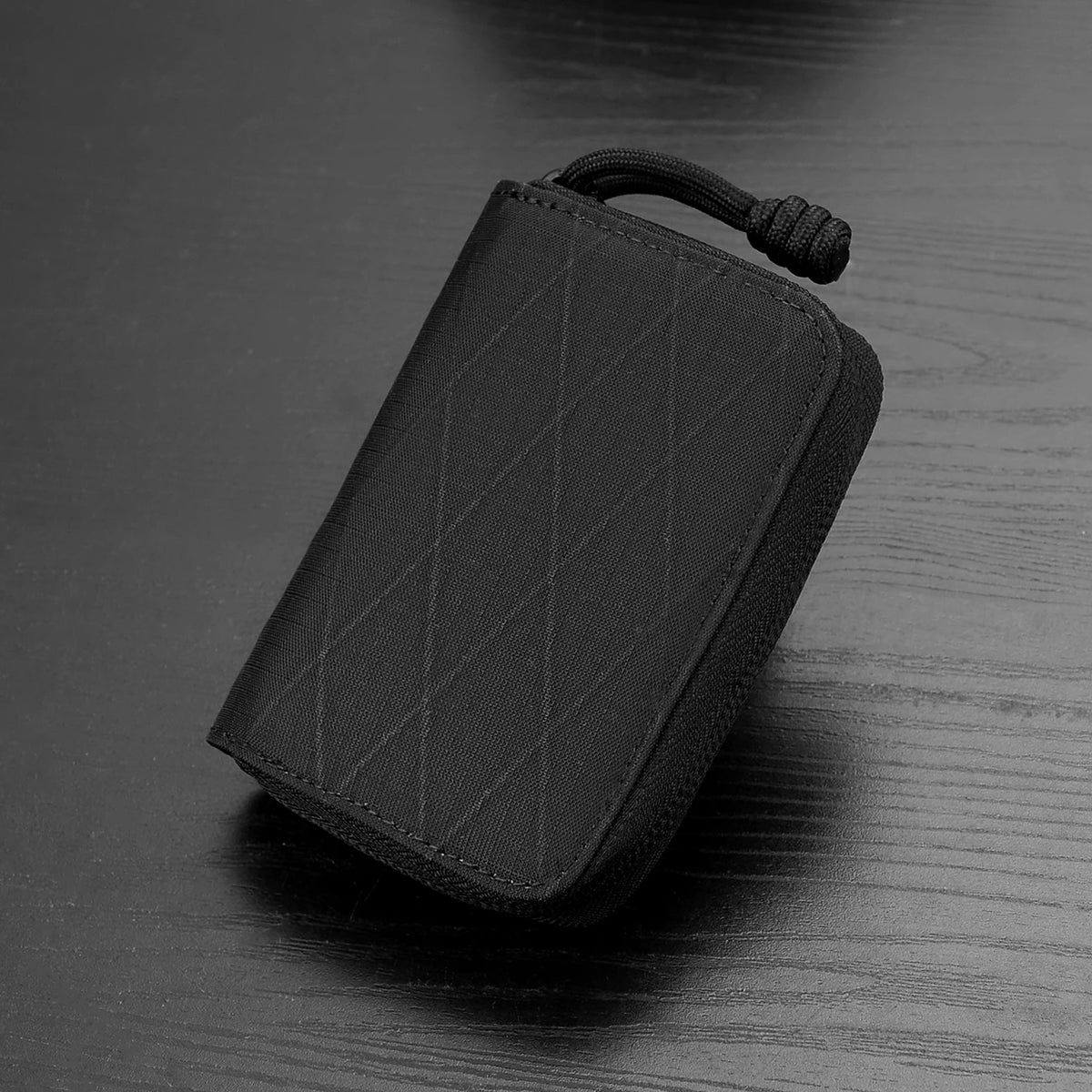 A black compact RFID wallet with a textured fabric is shown resting on a dark wooden surface.