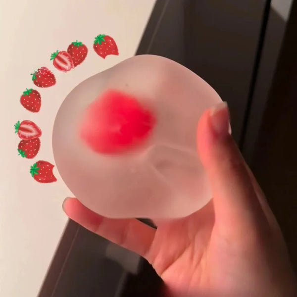 Une main tient une balle anti-stress transparente avec un motif de fraise rouge, montrant un mouvement de rebond lent.