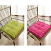 A thick corduroy floor cushion in lime green and magenta rests on a woven rattan chair.