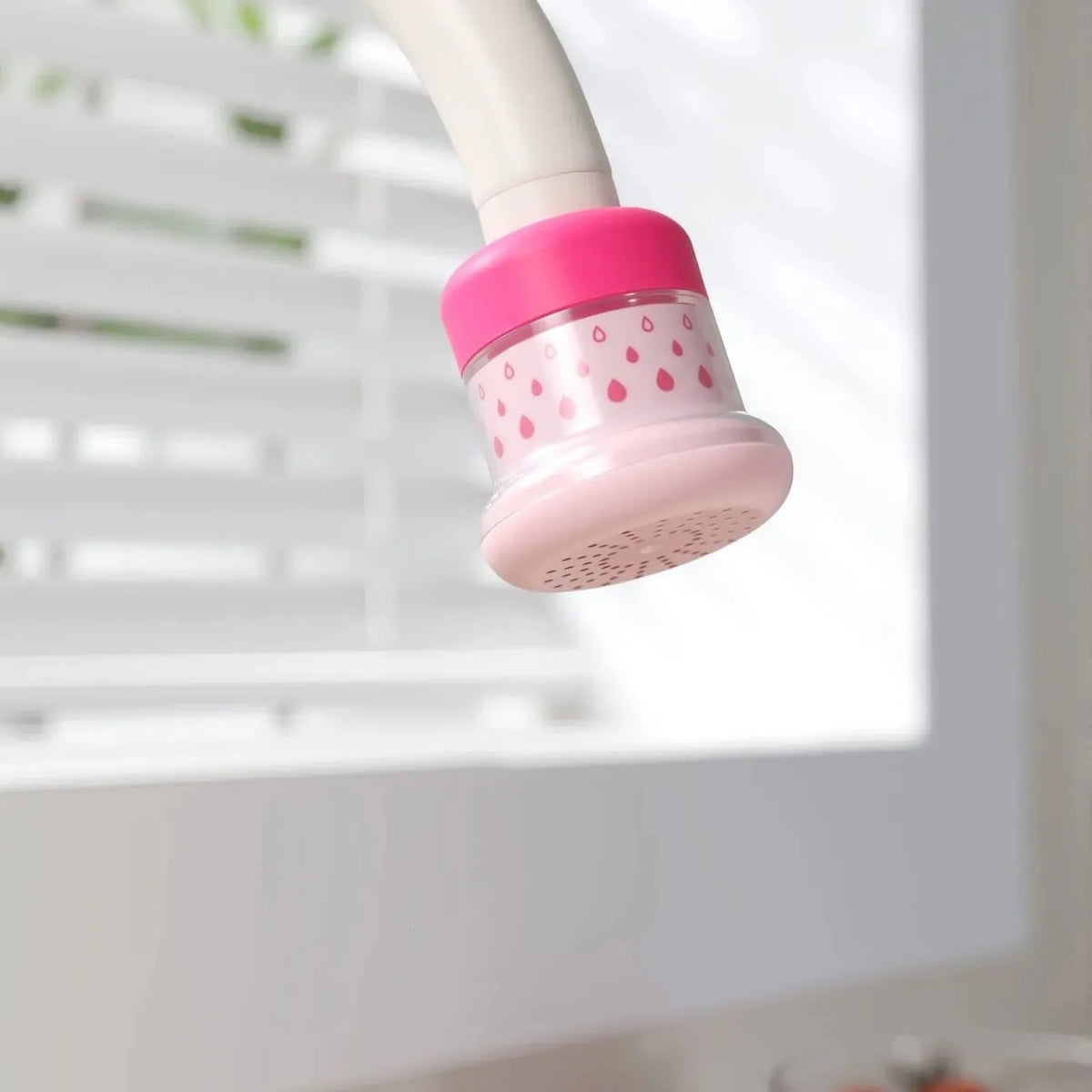 A pink kitchen faucet sprayer with a splash-proof water saving filter is shown hanging from a white pipe.