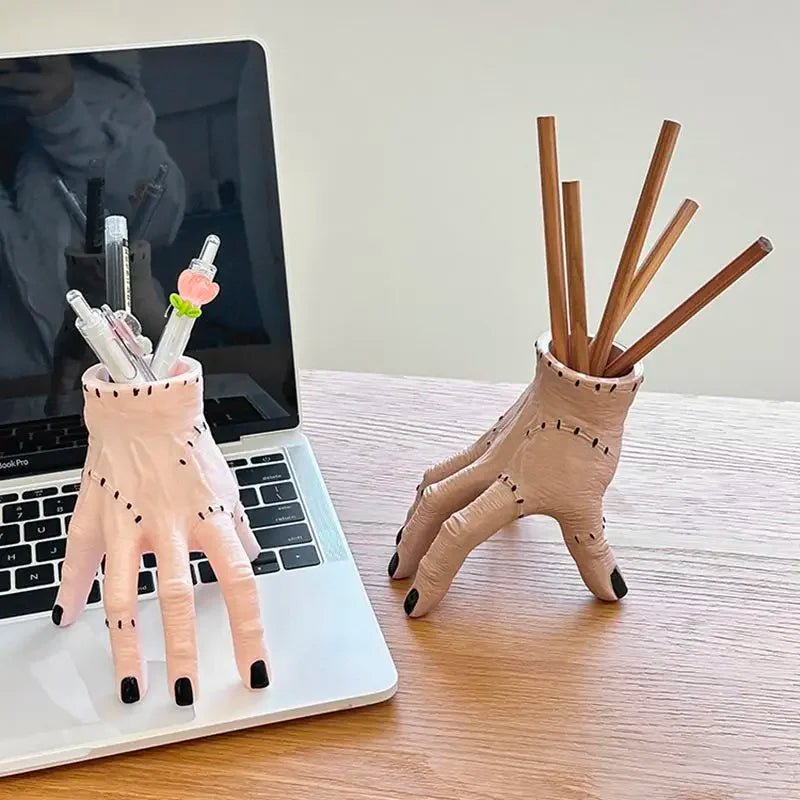 A beige resin hand planter and pen holder with wooden sticks is displayed next to a laptop.