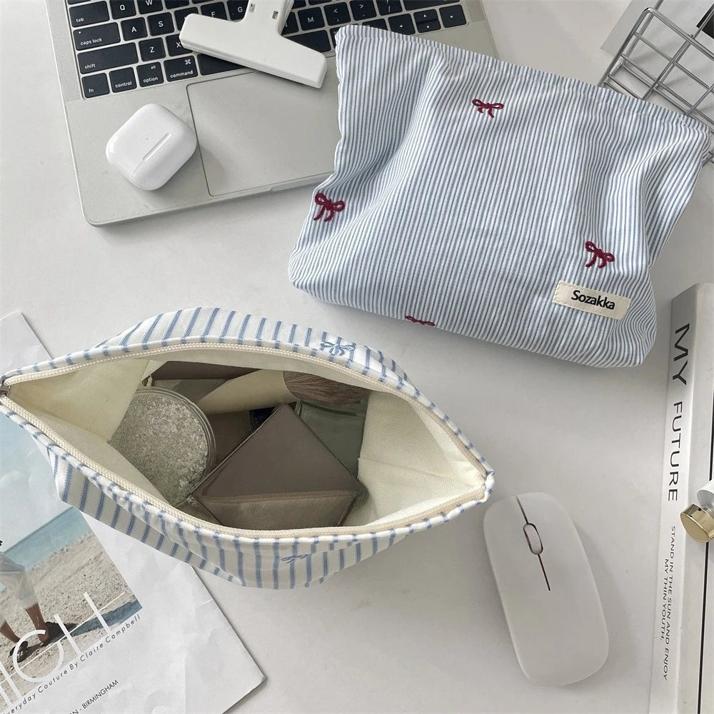 A light blue and white striped makeup bag is shown open, revealing a padded interior, next to a laptop and a wireless mouse.