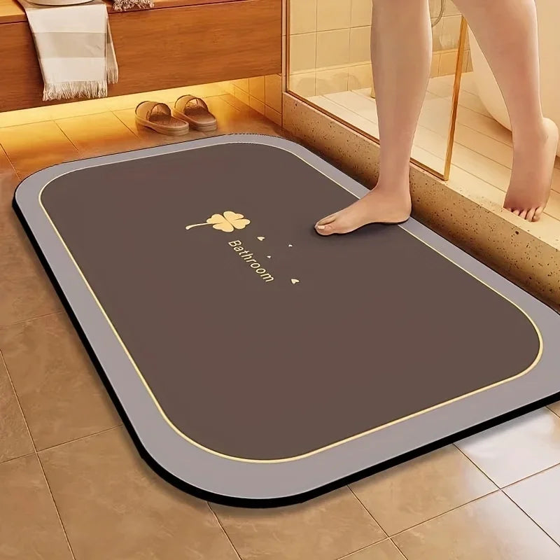A brown bathroom mat with a gold border and a small yellow flower design is placed on a tiled floor.