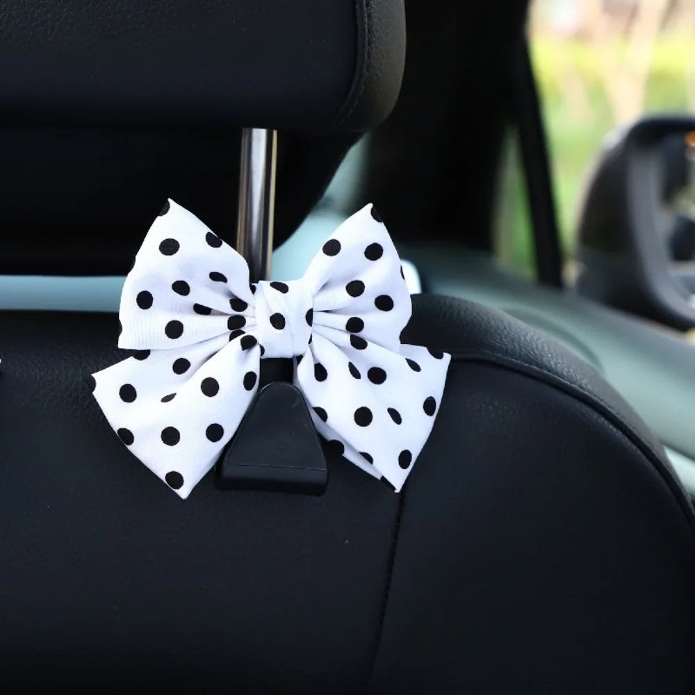 A white bow-shaped car seat back hook with black polka dots attached to a black car seat.