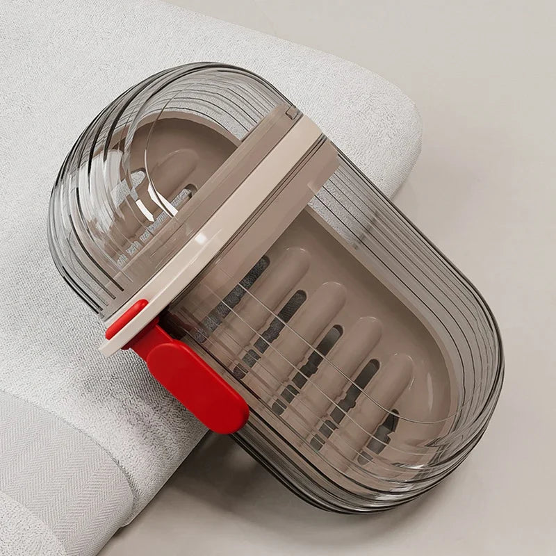 A clear portable travel soap box with a beige lid and red base is shown resting on a white cloth.