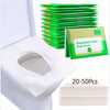 A stack of green disposable toilet seat covers is shown next to a white toilet, with another stack of pink covers displayed b