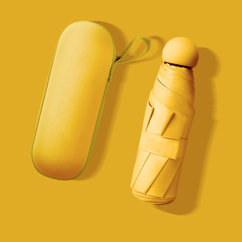A yellow compact 5-fold travel umbrella with a green strap is shown against a mustard yellow background.