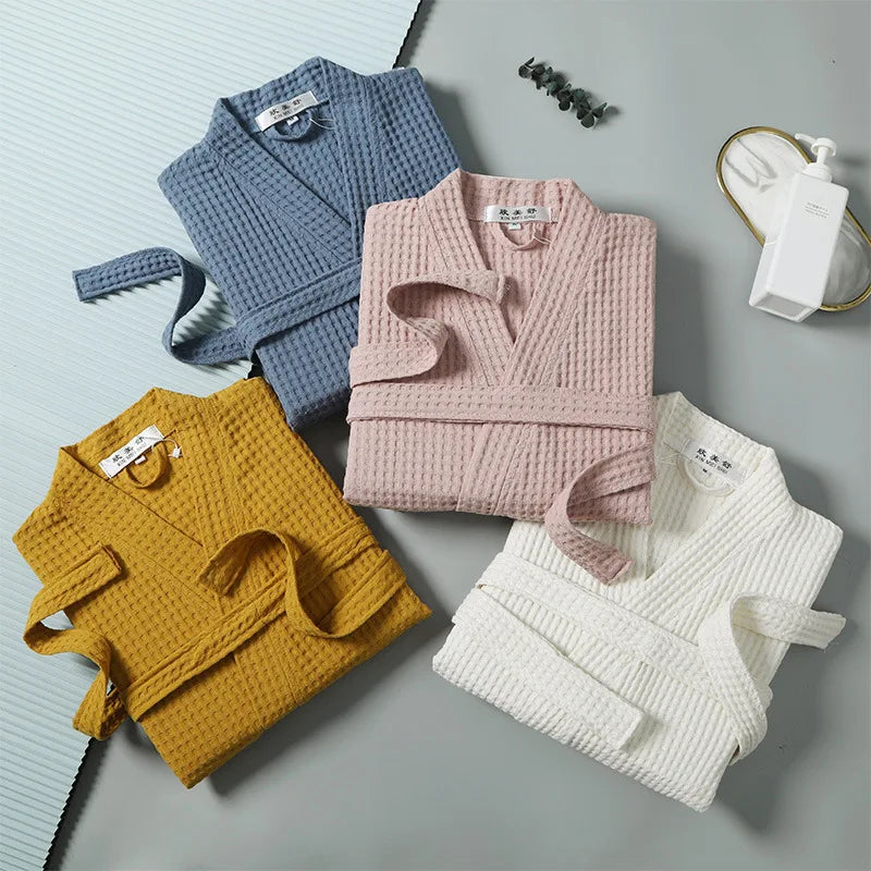 A collection of three knitted waffle texture robes in light blue, pink, and white laid out on a gray surface.