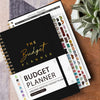 A spiral-bound budget planner with monthly and weekly pages and stickers is shown on a wooden surface.