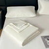 A white lightweight ice silk quilt is folded on a white bed with a white quilted pillow nearby.