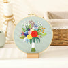 A circular embroidery hoop displaying a colorful floral design featuring various flowers and a white stem.