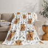 A beige flannel blanket featuring a pattern of Highland cows with floral and greenery accents.