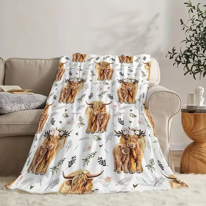A beige flannel blanket featuring a pattern of Highland cows with floral and greenery accents.