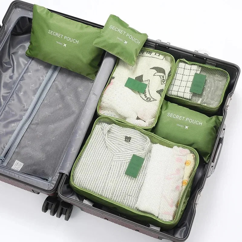 A set of six green and beige travel packing cubes and laundry pouches stored in a gray plastic case.