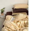 A set of minimalist striped 100% cotton duvet covers in beige and brown tones displayed on a bed.