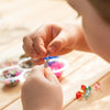 A child is using curved stainless steel beading needles to thread beads onto a string.