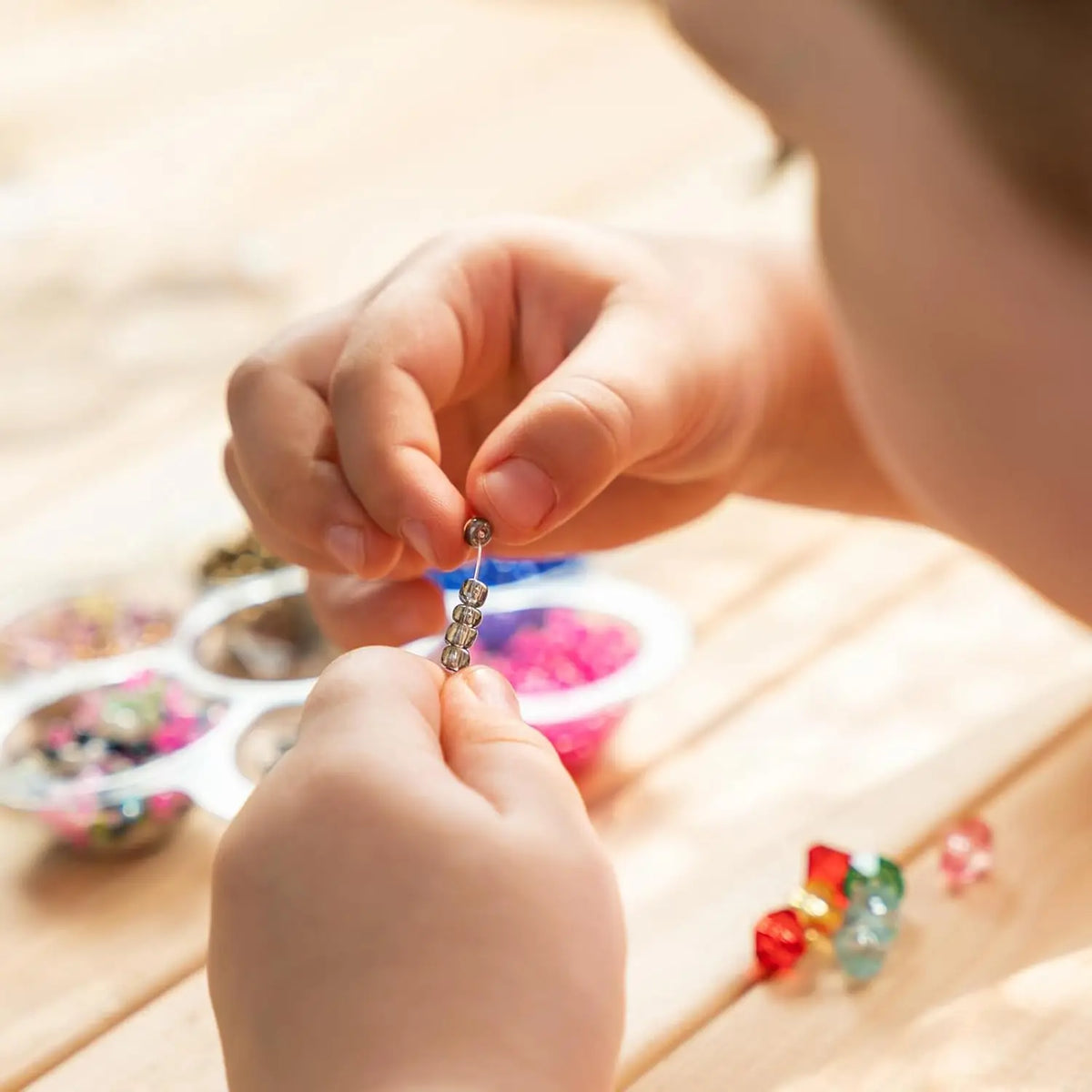 A child is using curved stainless steel beading needles to thread beads onto a string.