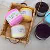 A wooden basket filled with various skeins of soft cotton yarn in pink, yellow, purple, and blue.