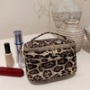 A dark brown leopard print cosmetic bag with a silver zipper resting on a white surface.