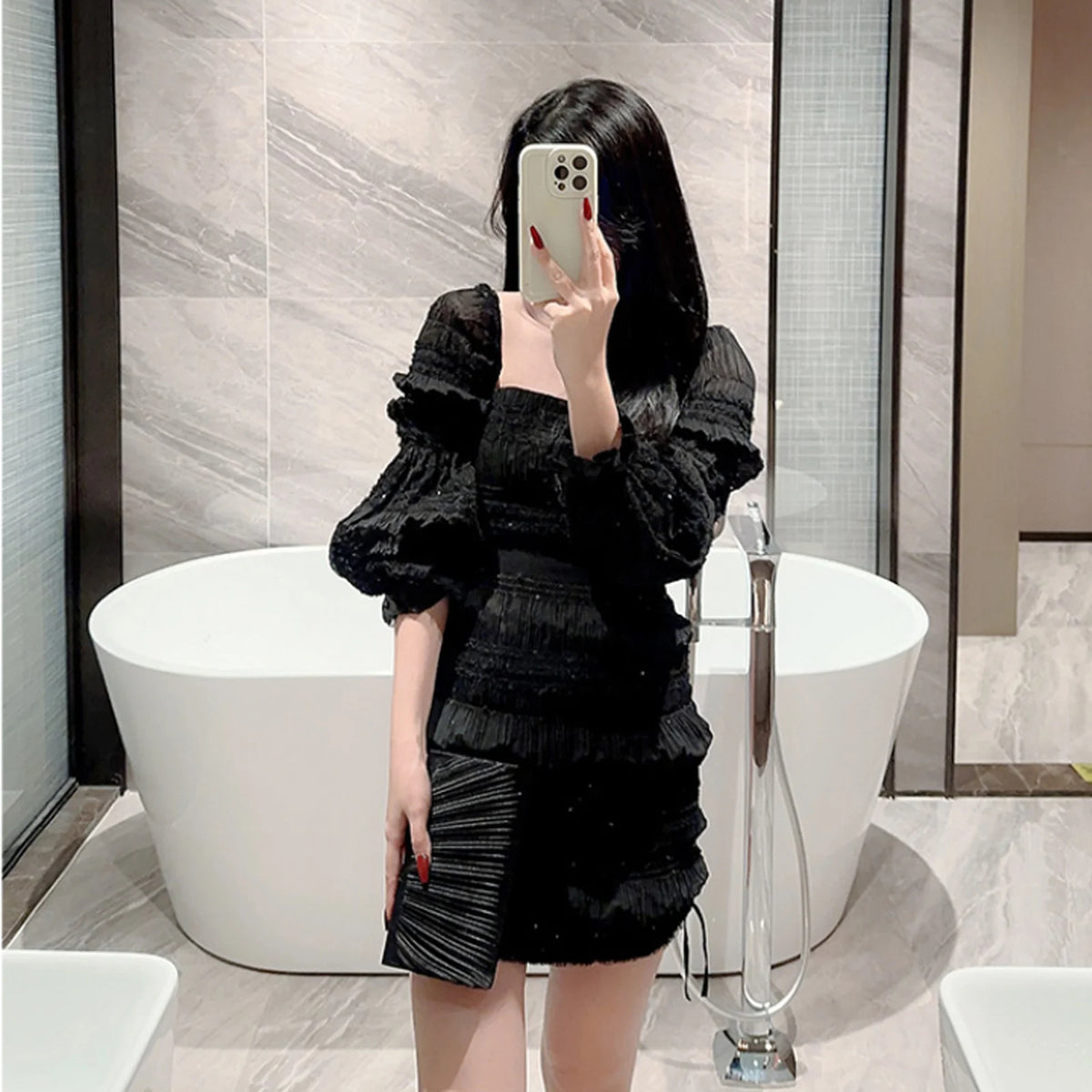 A woman in a black ruffled dress holds an elegant patent leather clutch bag with a chain strap.
