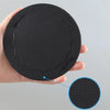 A hand holds a black exfoliating body scrub glove with a textured surface, showing a circular view of the product.