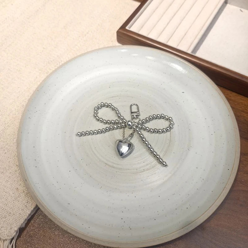 Silver pearl bow keychain with a heart charm resting on a white ceramic plate.