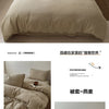 Ein Set faltiger beiger Baumwoll-Duvetcover und Kissen auf einem Bett.
