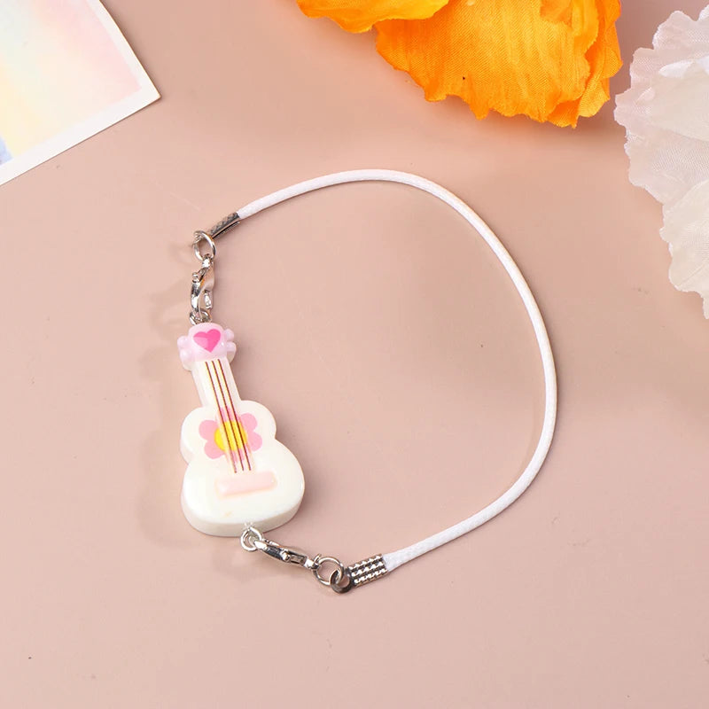 A white guitar-shaped bracelet with a pink flower detail and a silver clasp, displayed on a beige background.